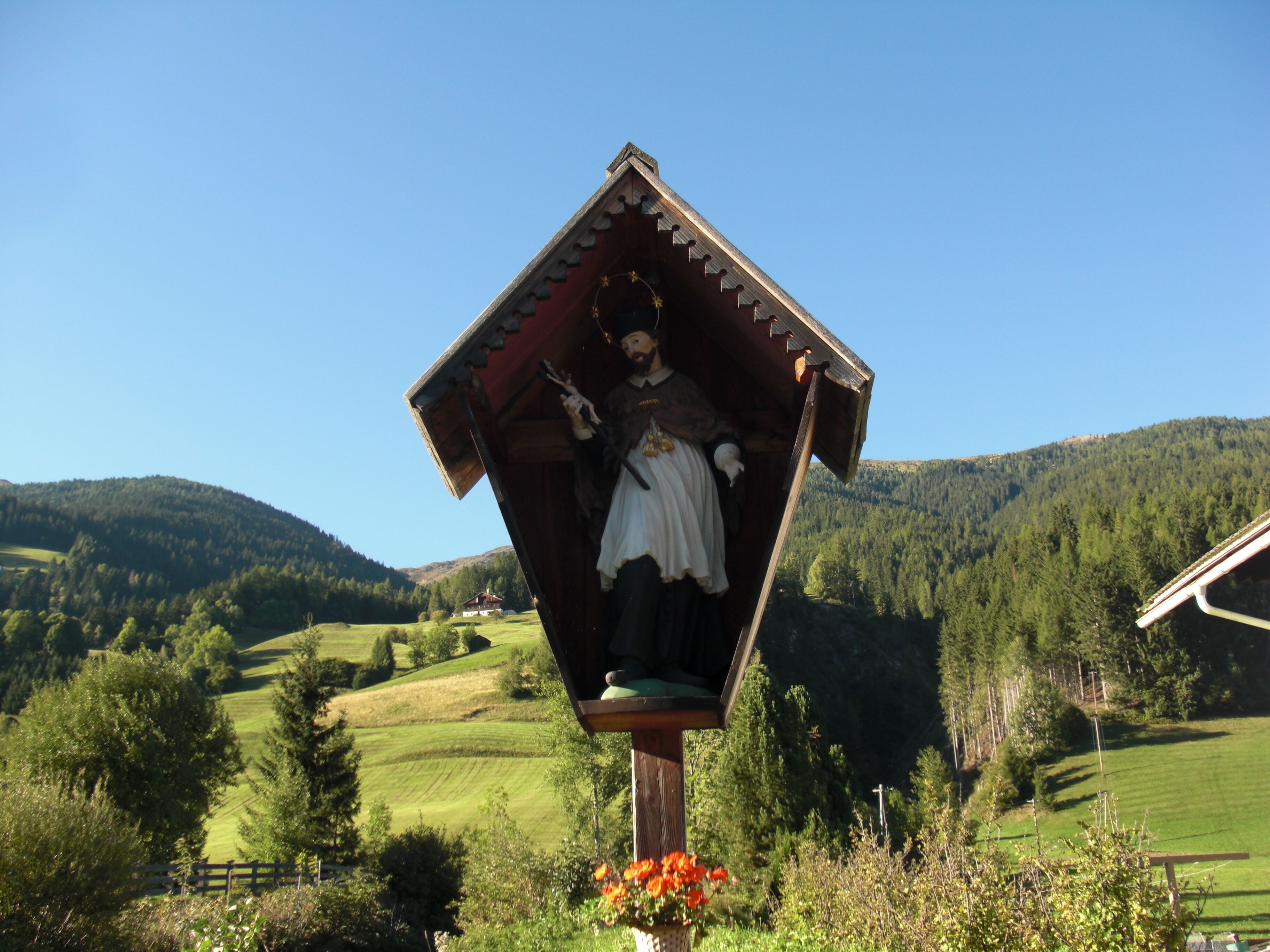 A wooden statue of a woman in traditional attire, surrounded by a rural landscape with rolling hills and a clear blue sky.