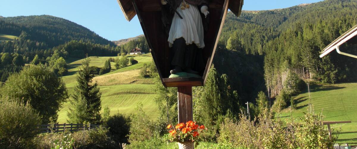 A wooden statue of a woman in traditional attire, surrounded by a rural landscape with rolling hills and a clear blue sky.