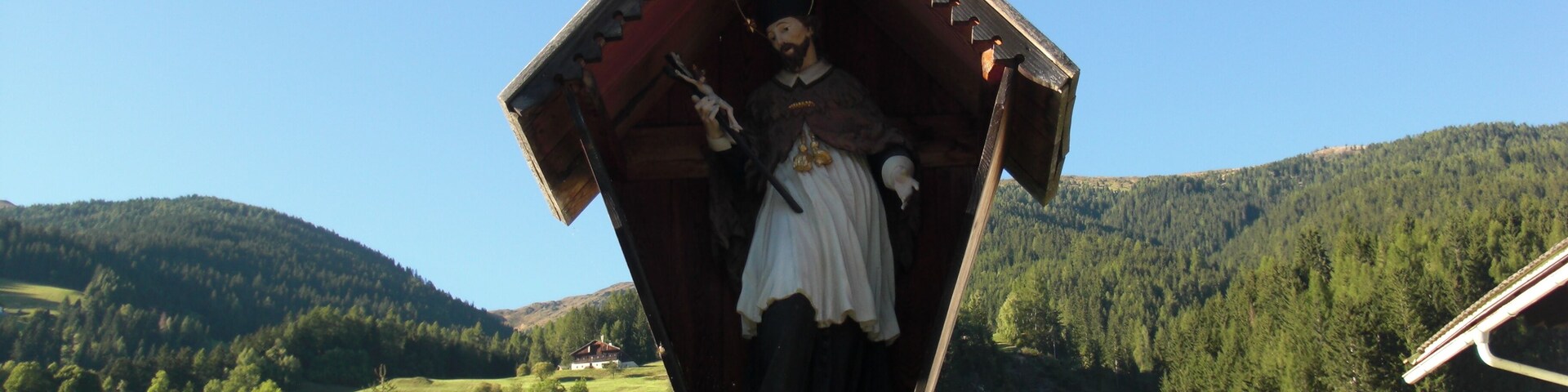 A wooden statue of a woman in traditional attire, surrounded by a rural landscape with rolling hills and a clear blue sky.