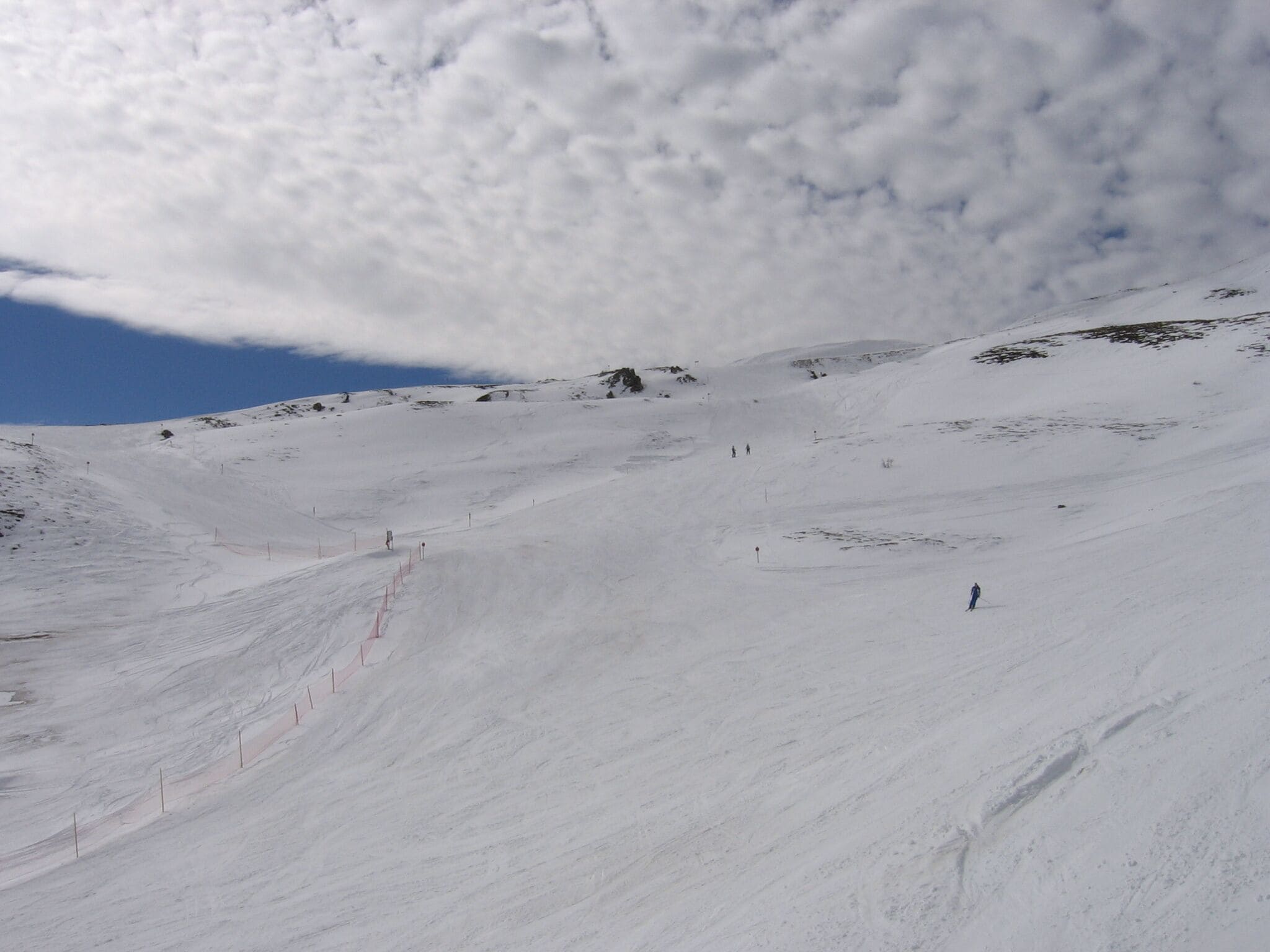 Pendiente nevada de una montaña con esquiadores y cielo despejado.