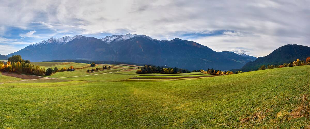 A green field with a winding path, mountains in the background, and autumn-colored trees.