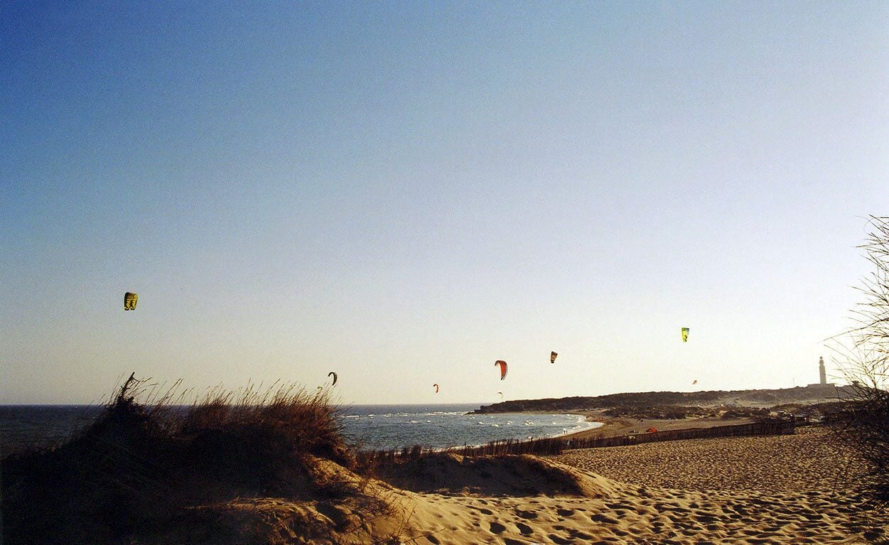A beach with sand dunes and a lighthouse in the distance.