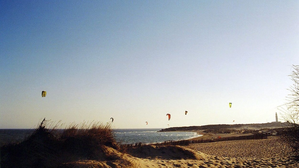 A beach with sand dunes and a lighthouse in the distance.