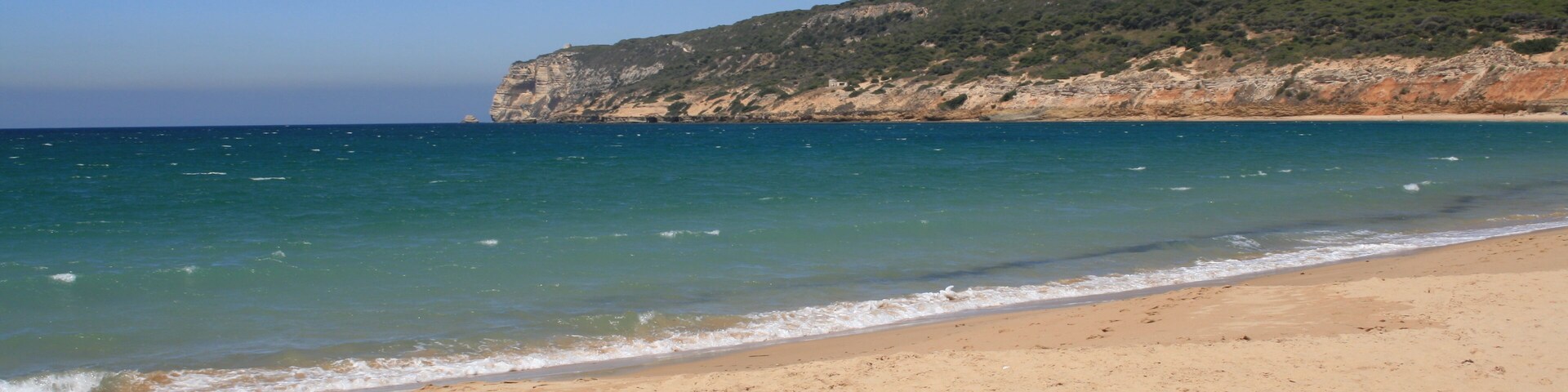Una playa arenosa con agua turquesa cristalina y un acantilado rocoso al fondo.