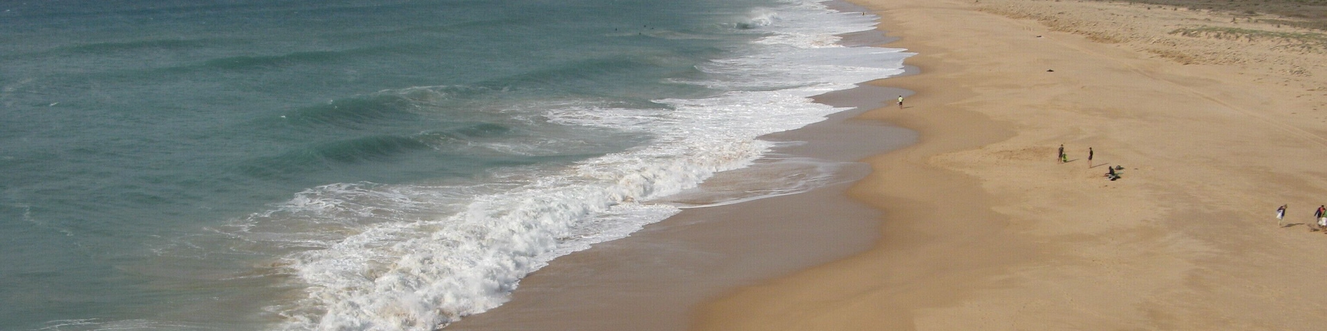 A sandy beach with gentle waves and a few people in the distance.