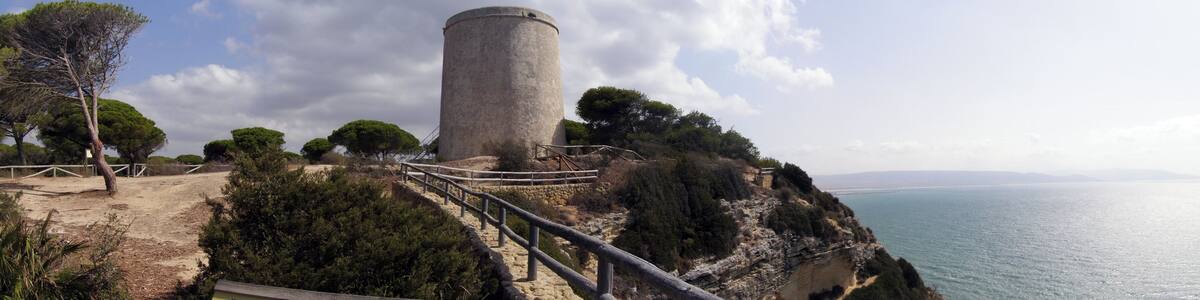 A coastal lighthouse on a cliff with a wooden walkway and a view of the sea.