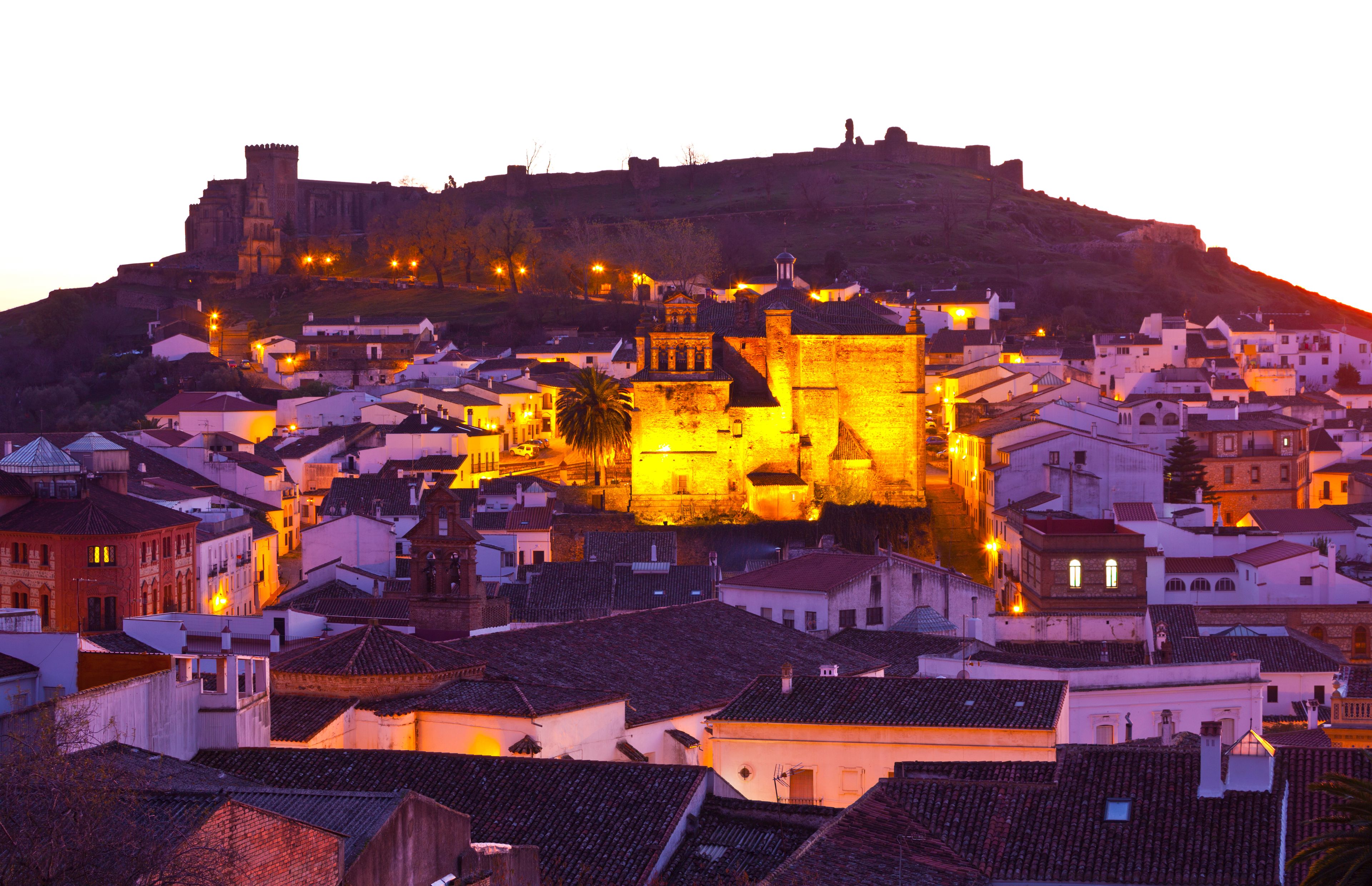 A historic town with a prominent castle on a hill, surrounded by white buildings with red-tiled roofs.