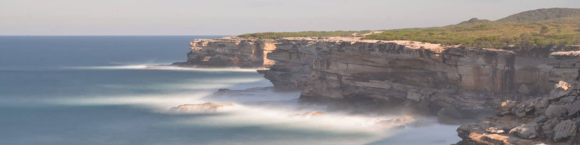 A coastal cliff with a rocky shoreline and a calm sea.