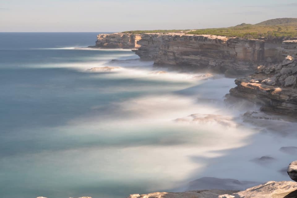 A coastal cliff with a rocky shoreline and a calm sea.