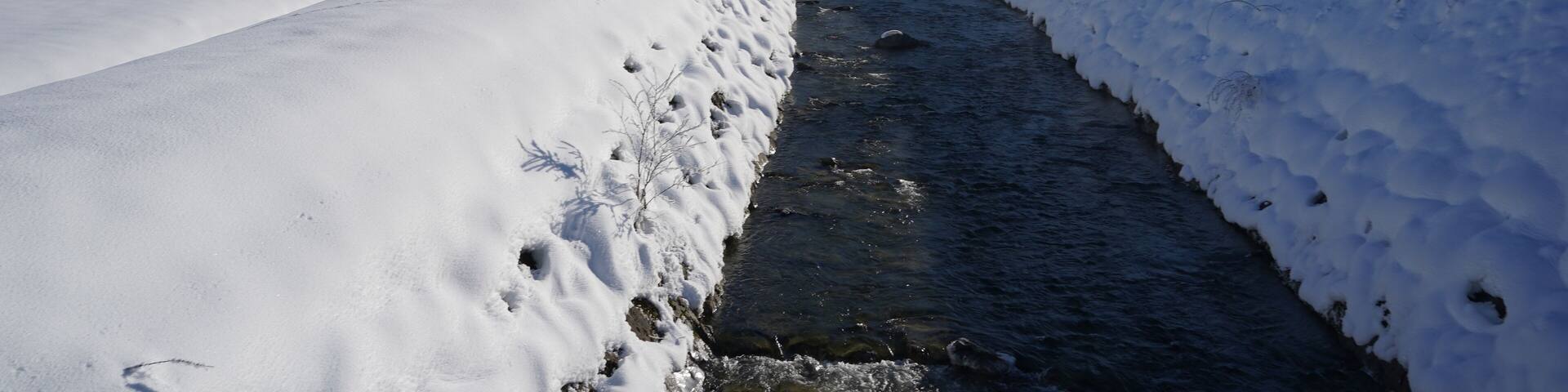 Stream or brook in winter. It has both banks thickly covered with snow and disappears in perspective. The brook flows in the cross country skiing region Studen in Switzerland.