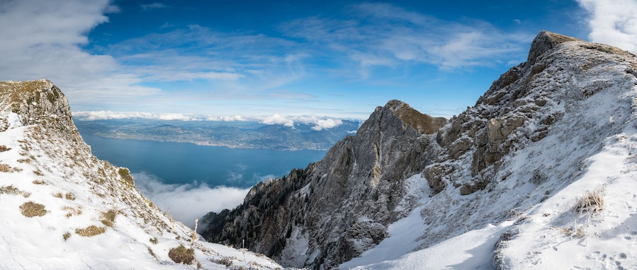 Pico de montanha coberto de neve, com um lago e paisagem urbana ao longe.