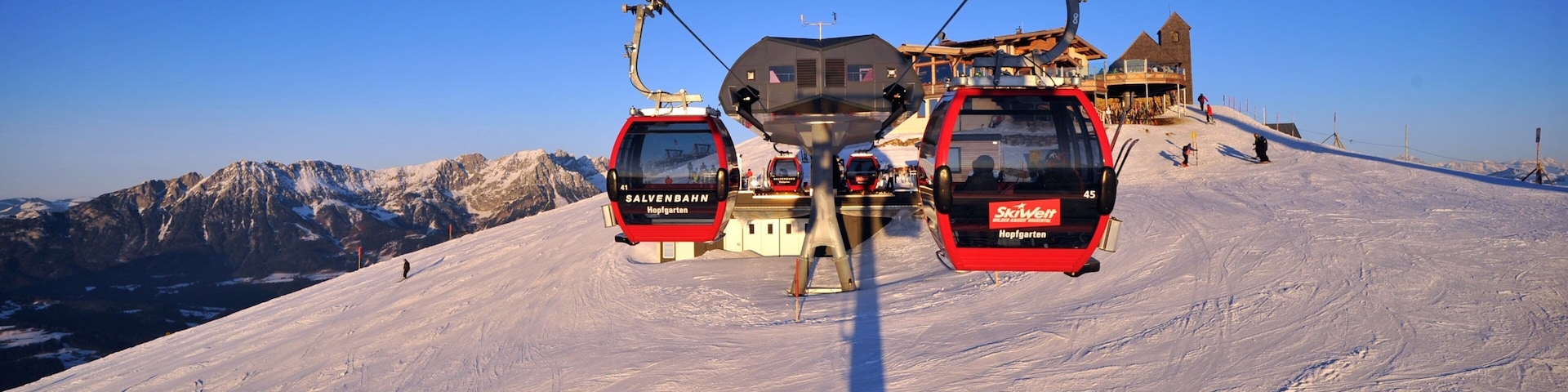 A ski lift with two red gondolas, a mountain backdrop, and a building with a tower.