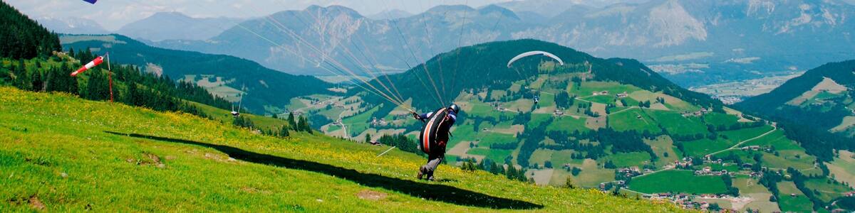 Un parapente descend une colline herbeuse, avec un paysage montagneux en arrière-plan.