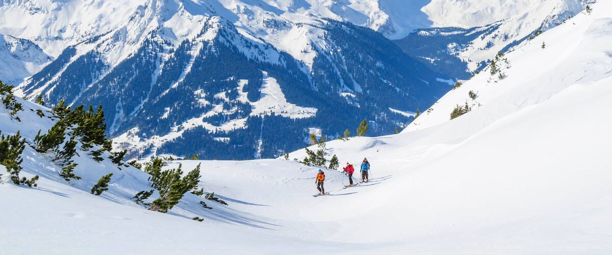 A snowy mountain landscape with three skiers descending a slope.