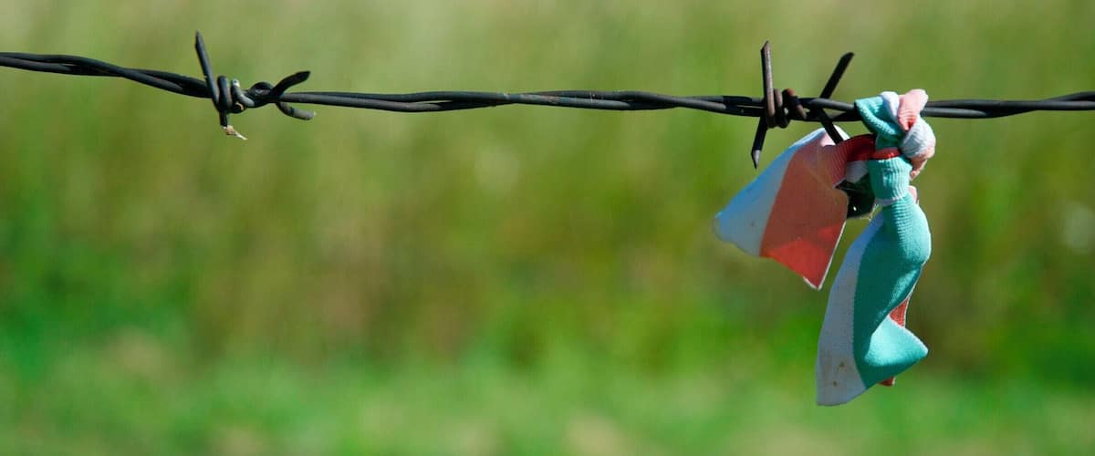 A barbed wire with a colorful flag and a small figure hanging from it.