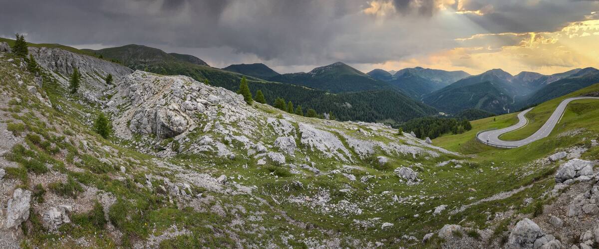 A winding mountain road with rocky terrain and green hills.