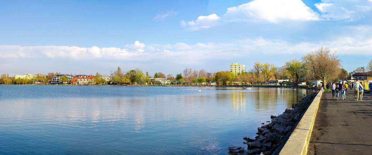 A calm river with a stone embankment and a row of buildings along the opposite bank.