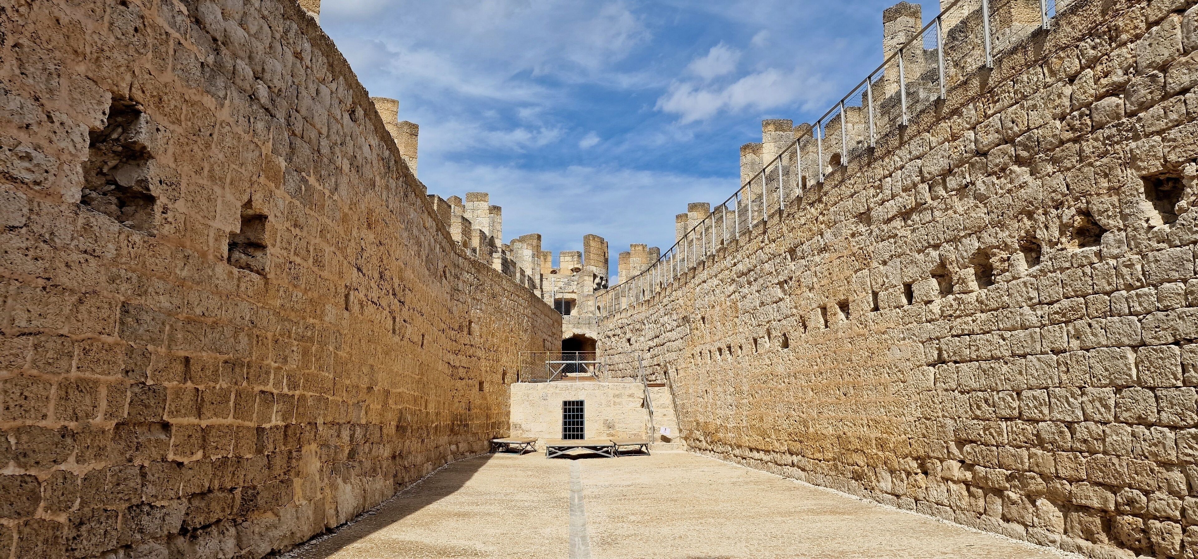 A narrow stone corridor with high walls and a clear sky.