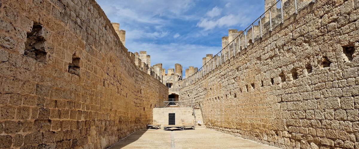 A narrow stone corridor with high walls and a clear sky.