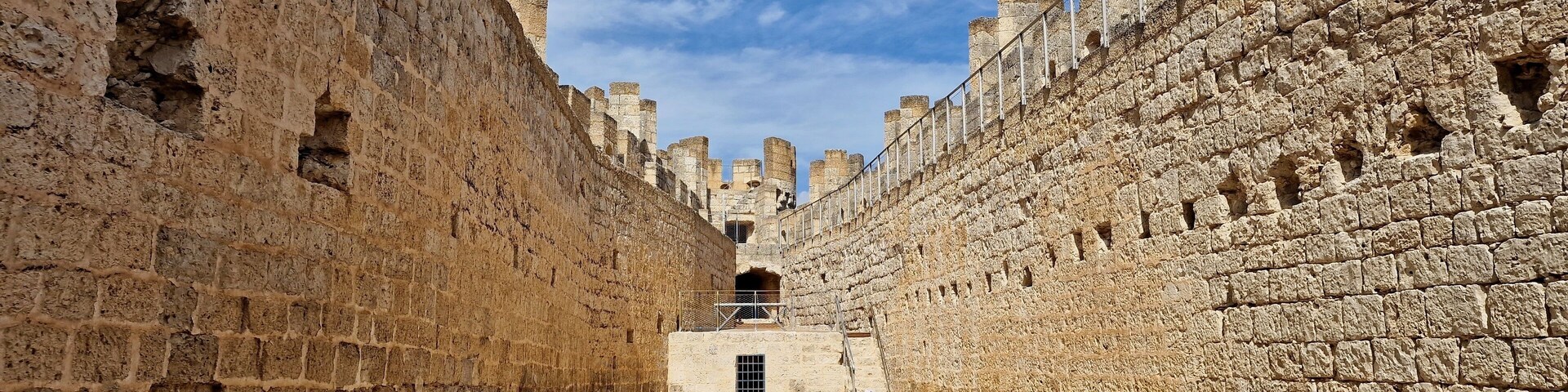 A narrow stone corridor with high walls and a clear sky.