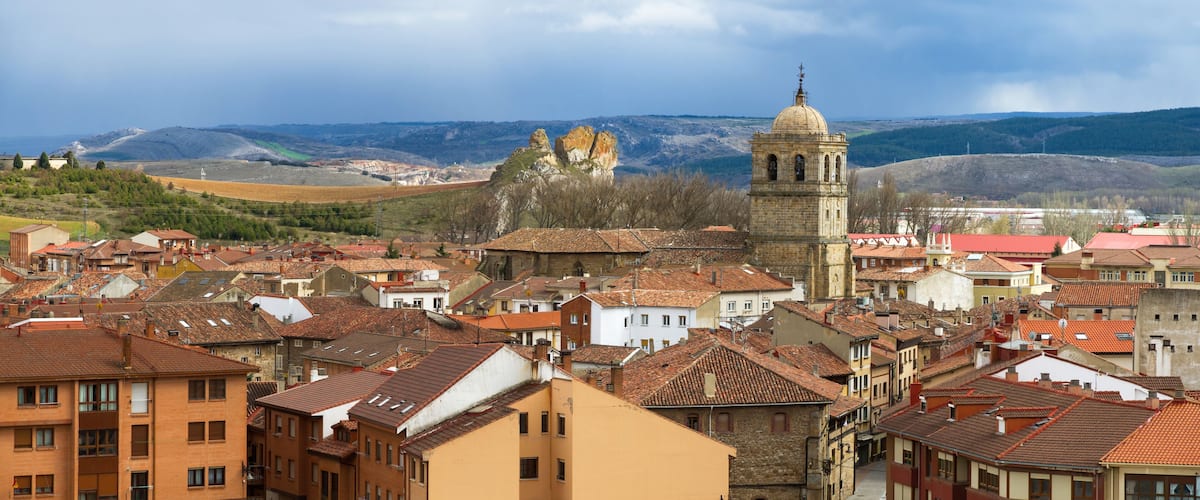 A town with historic buildings, a prominent church, and rolling hills in the background.