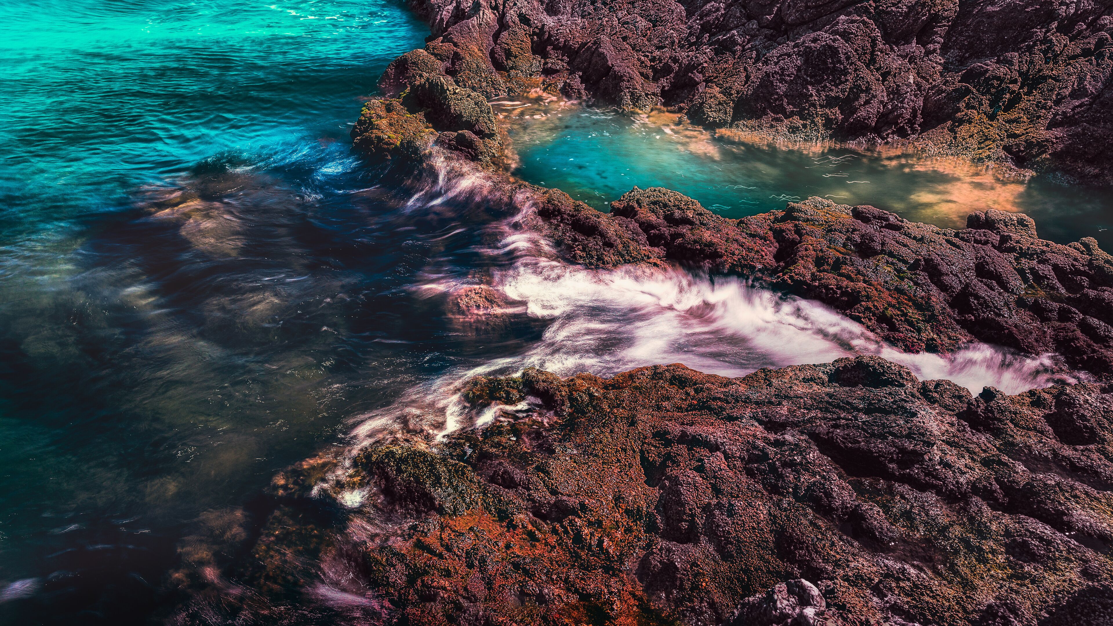 Una costa rocosa con aguas turquesas cristalinas y olas rompiendo contra las rocas.