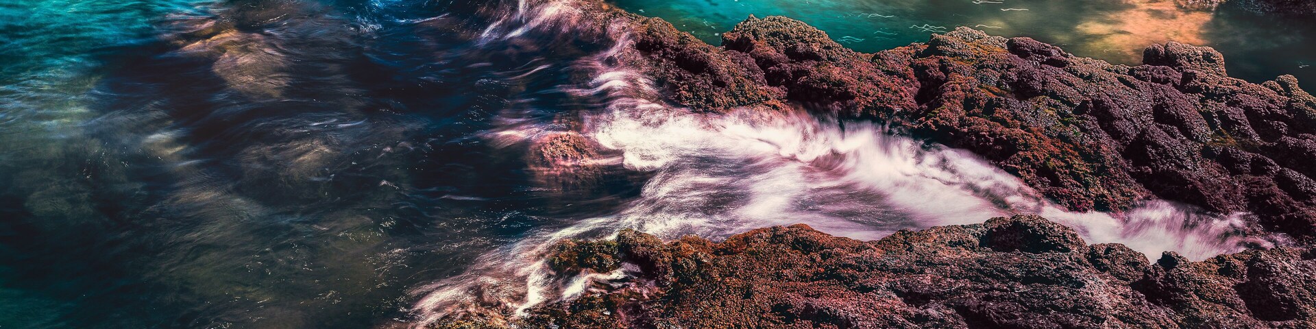 Una costa rocosa con aguas turquesas cristalinas y olas rompiendo contra las rocas.