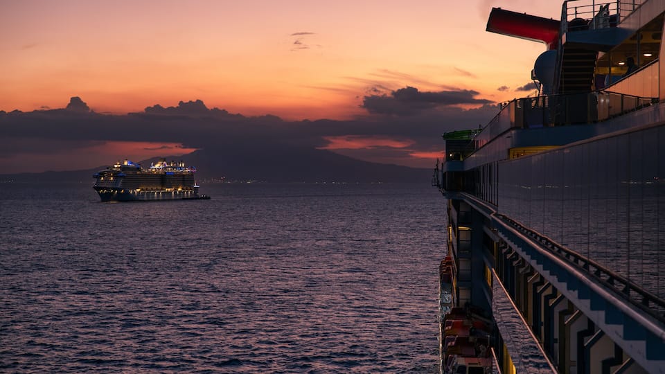 A cruise ship at sunset with a bridge extending over the water.