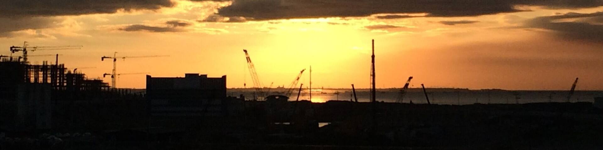 A sunset over a construction site with cranes and a bridge.