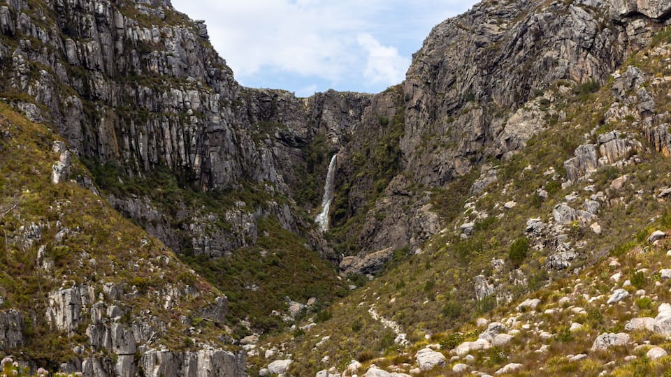 A mountainous landscape with a waterfall cascading down a rocky gorge.