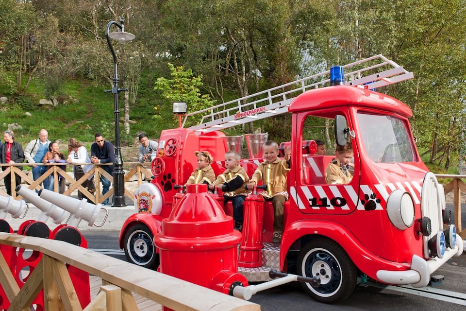 A red fire truck with children riding in the back, surrounded by spectators.