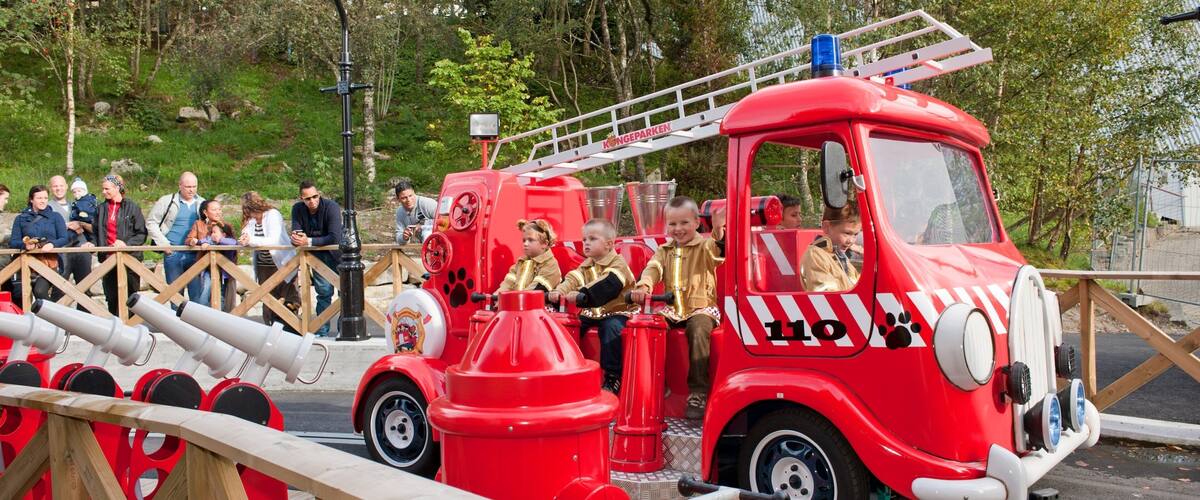 A red fire truck with children riding in the back, surrounded by spectators.