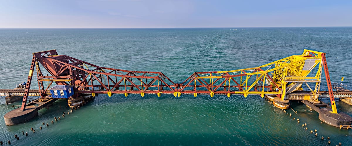 A large industrial structure spanning a body of water, with a blue building and yellow and red metal framework.