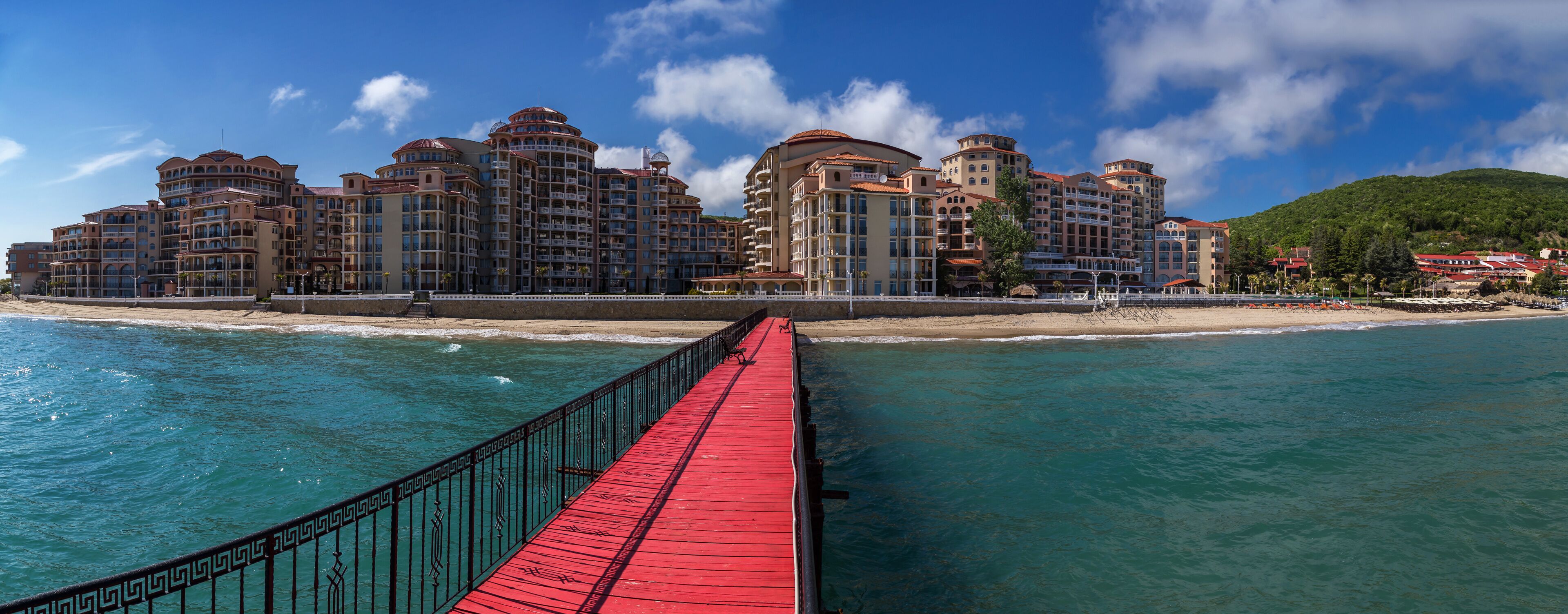 A coastal resort with a red pier leading to a beachfront hotel complex.