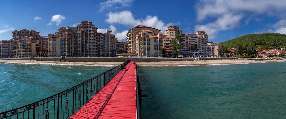 A coastal resort with a red pier leading to a beachfront hotel complex.