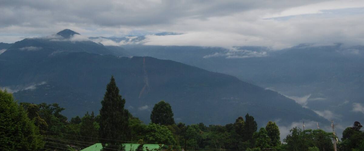 A mountainous landscape with dense forests and a cloudy sky.