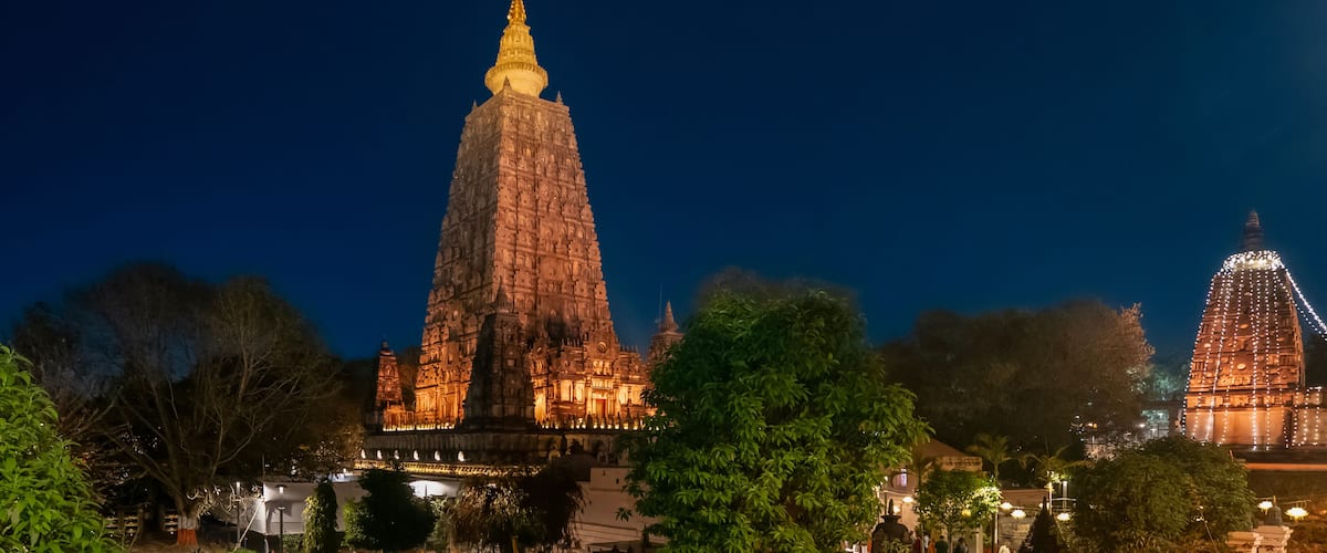 A large temple with a golden spire, surrounded by trees and illuminated by lights.