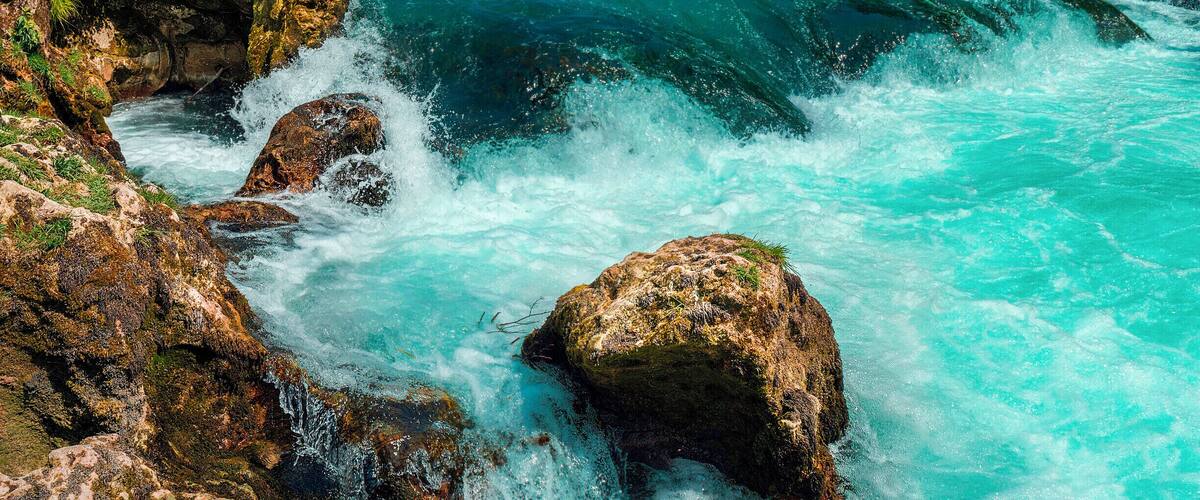 A waterfall cascading over rocks into a turquoise river surrounded by lush greenery.