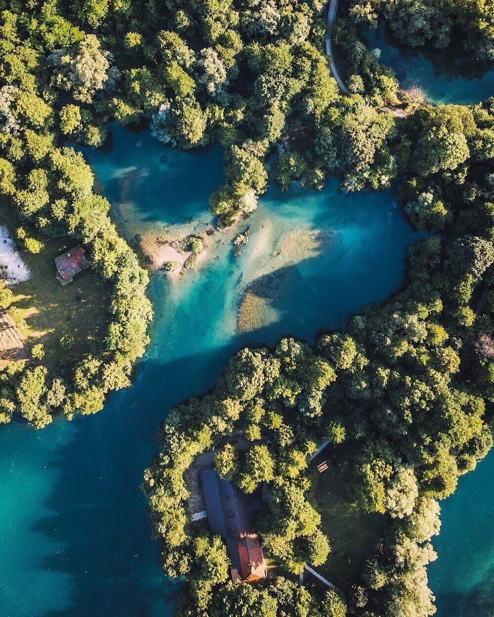 An aerial view of a coastal area with clear blue waters, dense green forests, and a small settlement with visible buildings.