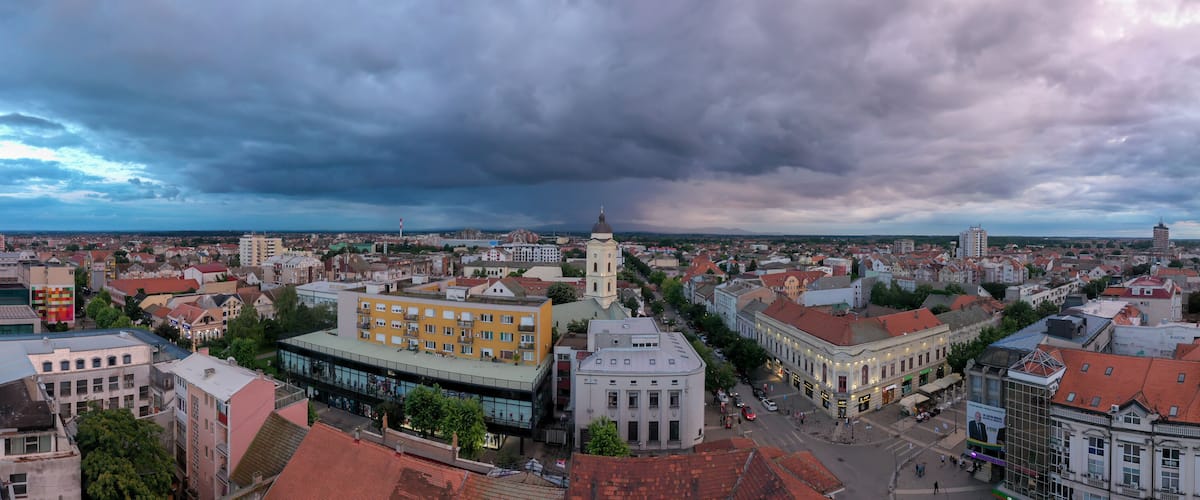 A cityscape with a prominent church tower, a mix of historic and modern buildings, and a cloudy sky.