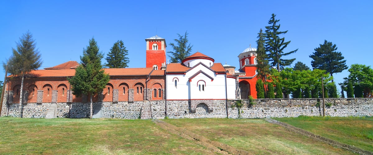 A church with a red and white facade, a bell tower, and a stone wall.