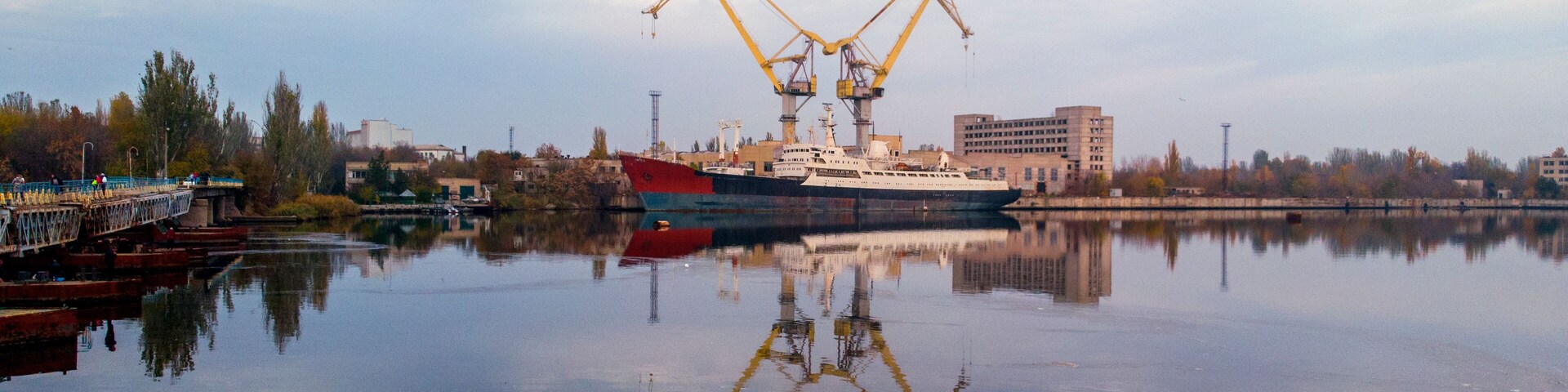 Um grande navio de carga atracado em um porto, com guindastes e edifícios ao fundo.