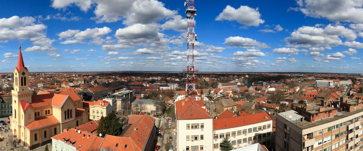 A panoramic view of a city with historic buildings, a prominent church with a tall spire, and a telecommunications tower.