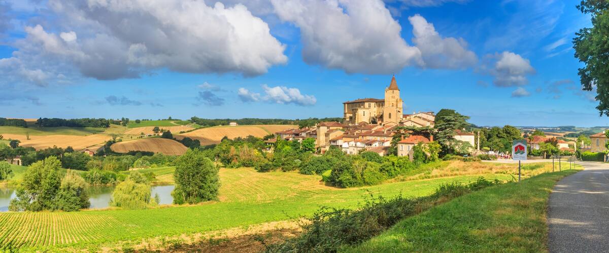A historic town with a prominent church, rolling fields, a river, and a clear sky.