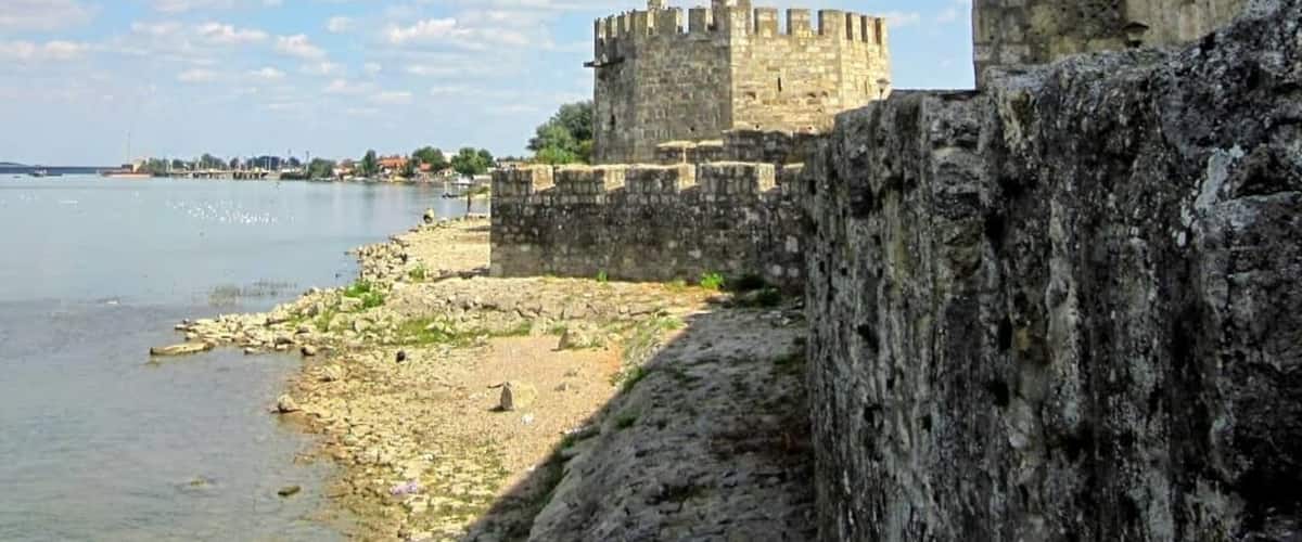A stone castle by a calm body of water with a clear sky.