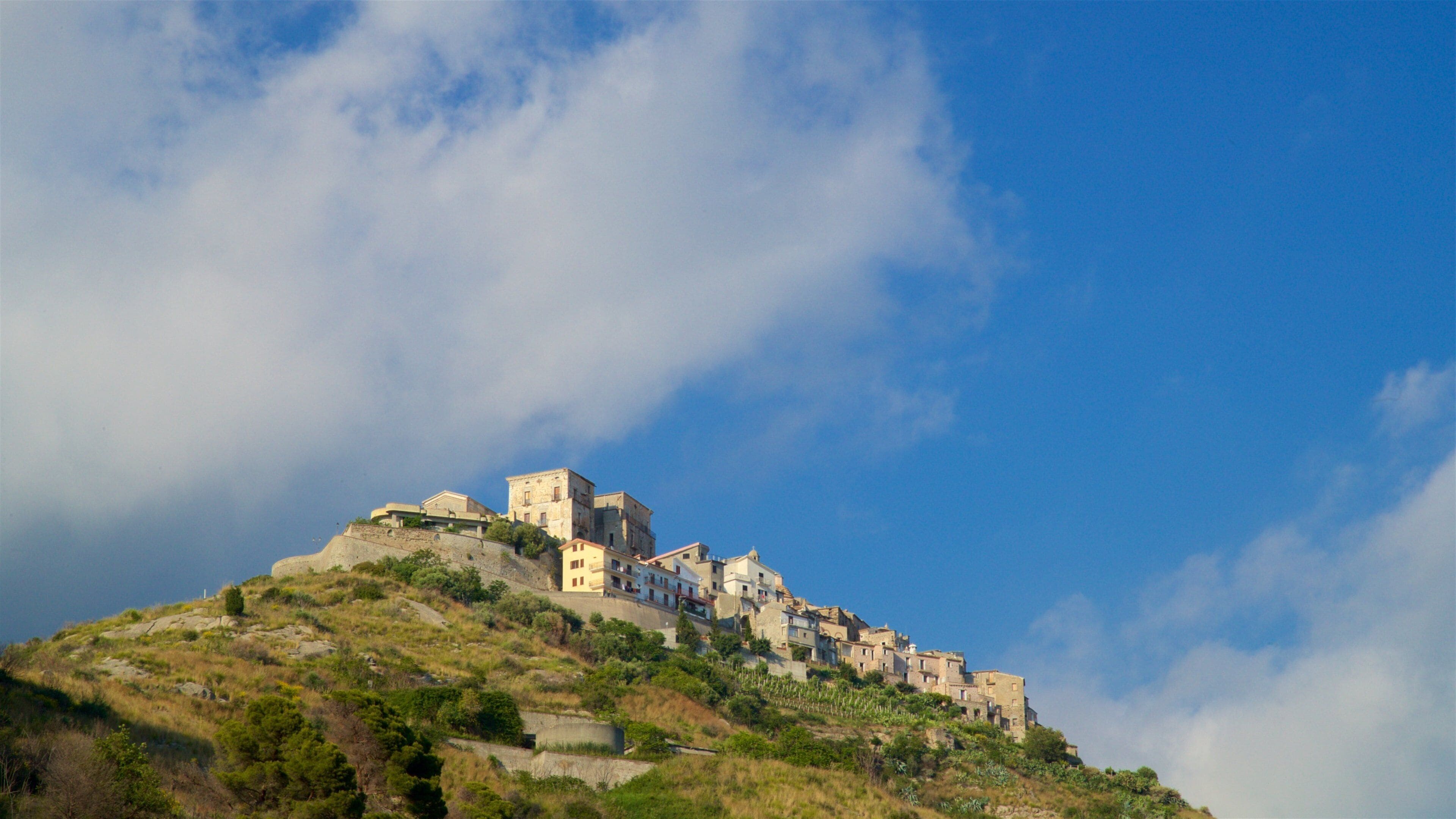 A hillside settlement with buildings perched on a slope under a partly cloudy sky.