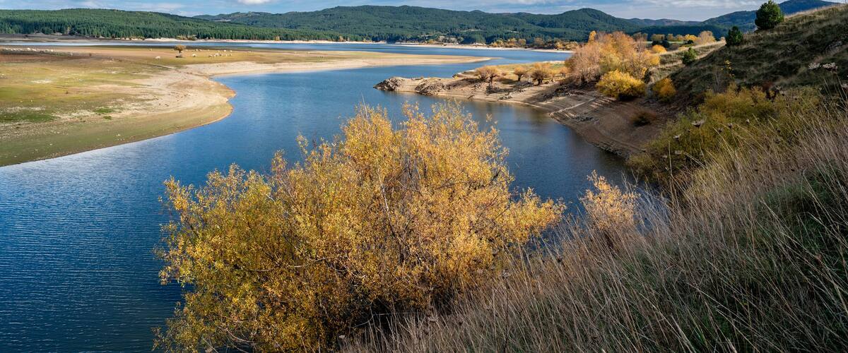 A river winding through a hilly landscape with autumn foliage and distant mountains.