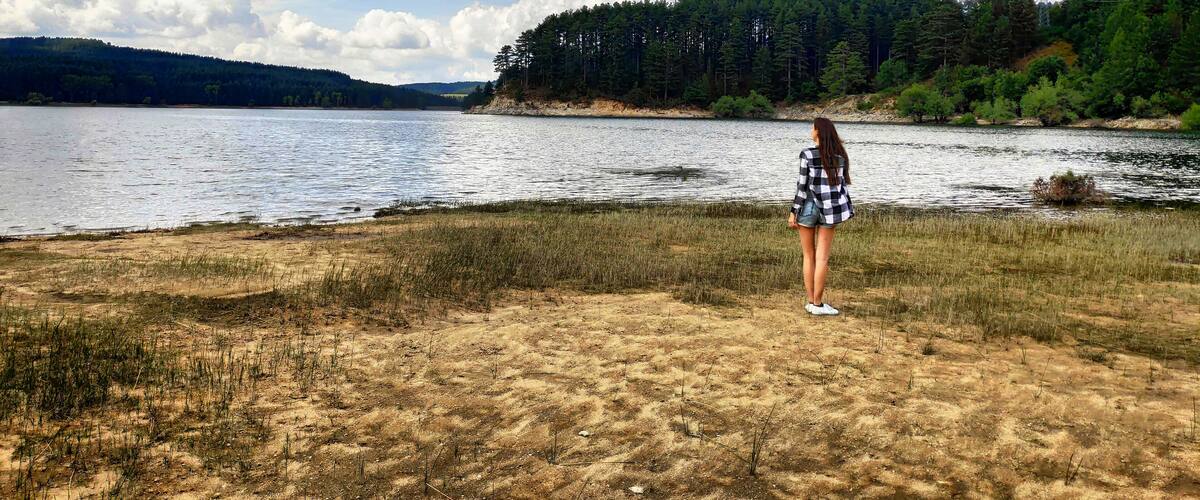 A person standing by a lake with a forested hill in the background.