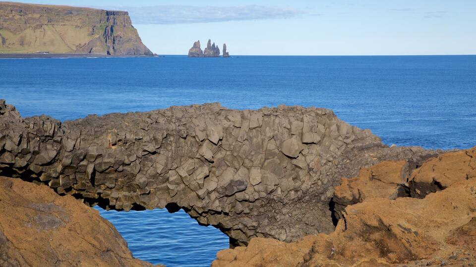 A rocky coastal landscape with a prominent arch formation and distant rocky formations in the sea.