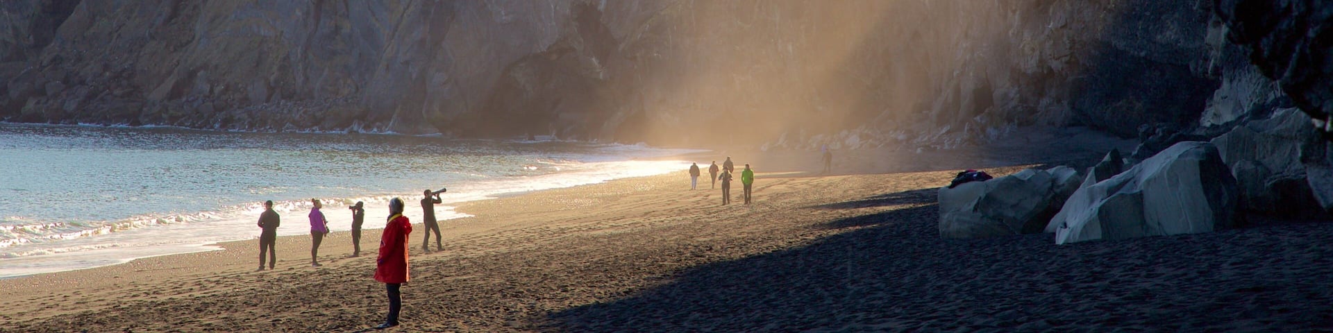 A coastal scene with a rocky cliff, a beach, and a lighthouse in the distance.